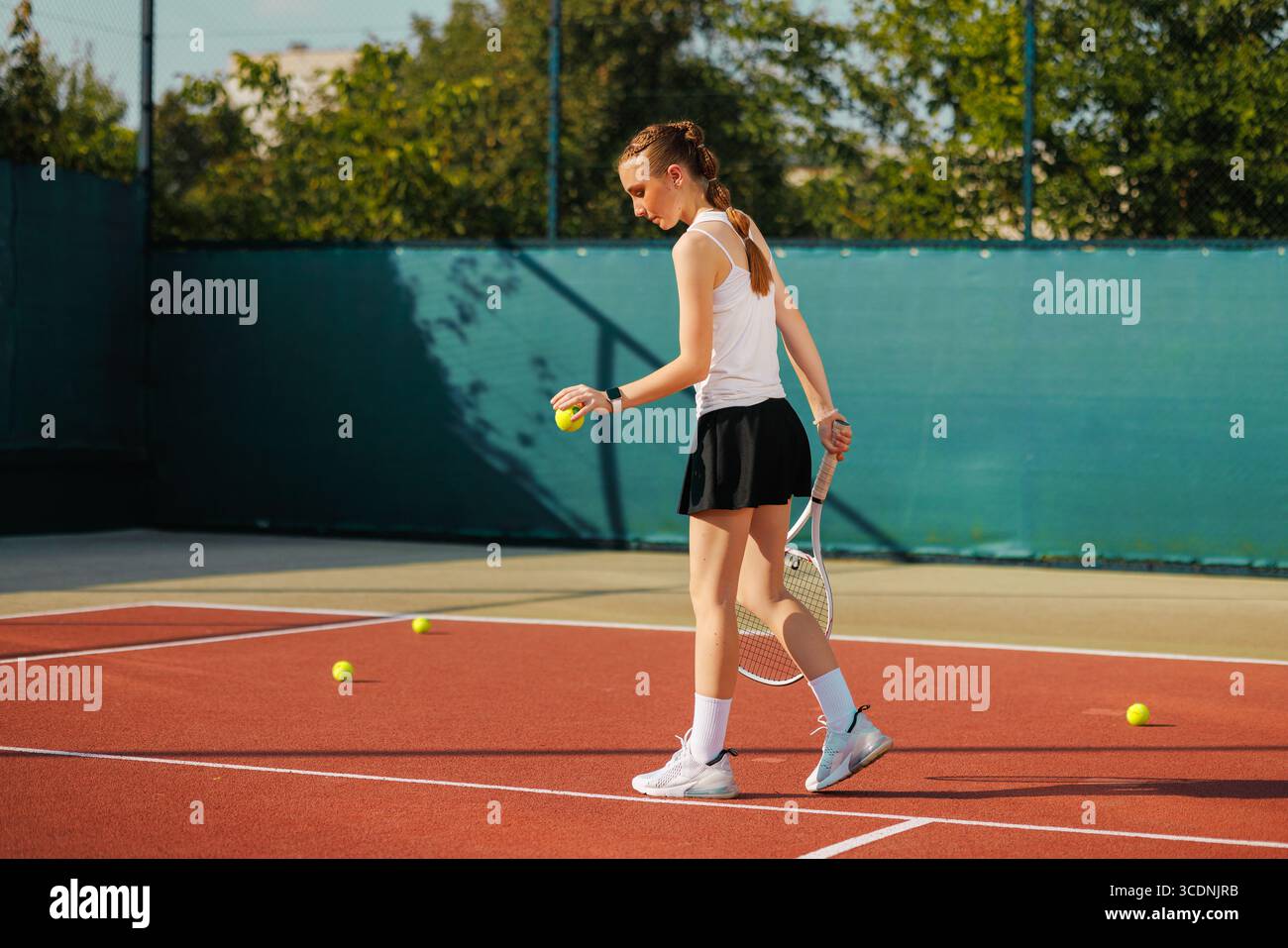 La tennista Teen Girl raccoglie palline durante le esercitazioni all'aperto, concentrandosi sull'allenamento, la motivazione e l'energia sportiva giovanile Foto Stock