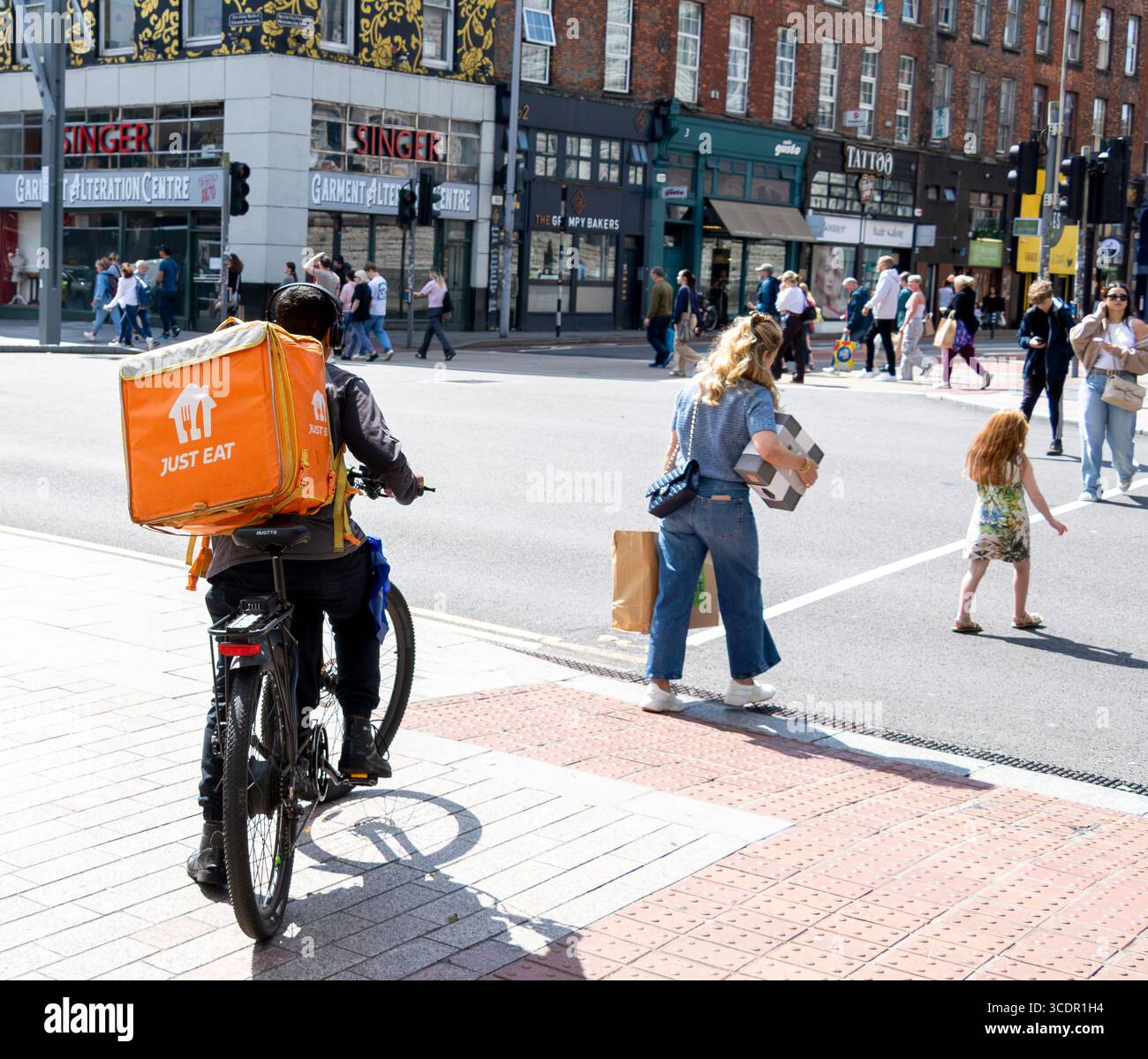 Consegna di fast food in bicicletta in attesa di attraversare strade trafficate, Cork City, Irlanda Foto Stock