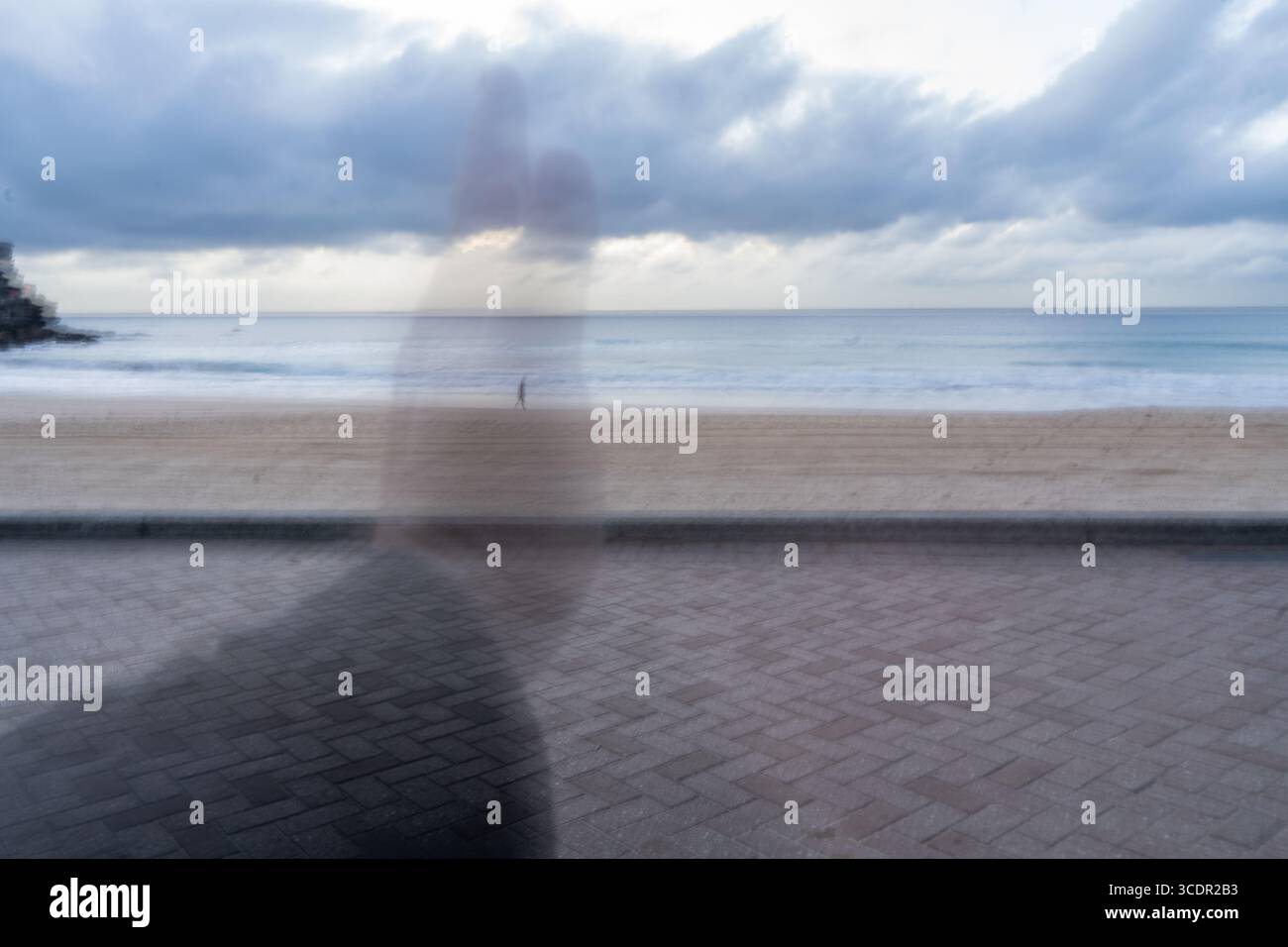 Immagine astratta di una persona che cammina su una spiaggia, visibile attraverso una mano trasparente Foto Stock