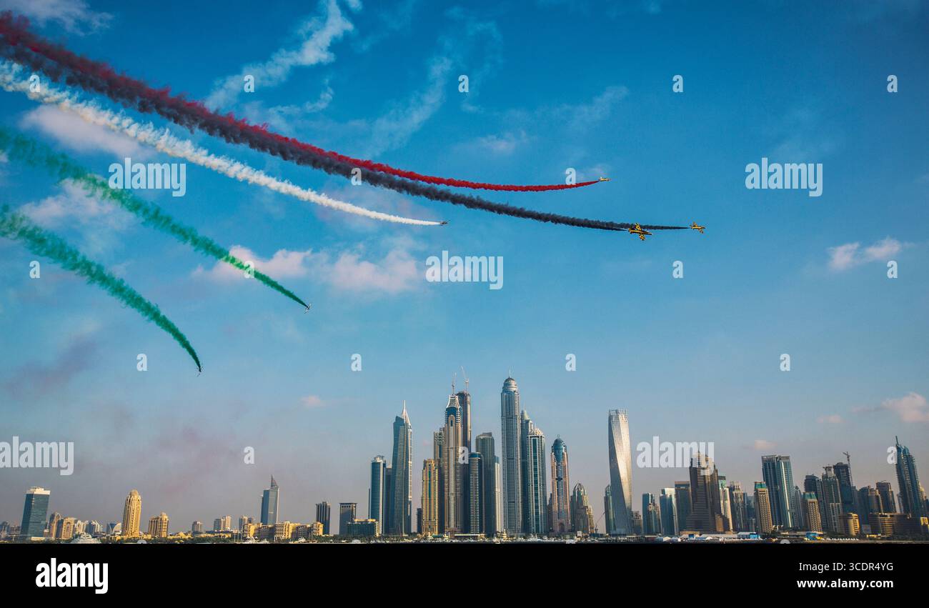 Aerei acrobatici colorati che volano sopra lo skyline di Dubai con sentieri per fumo bandiera degli Emirati Arabi Uniti, cielo blu, festa nazionale, paesaggio urbano moderno, spettacolo dell'aviazione. Foto Stock