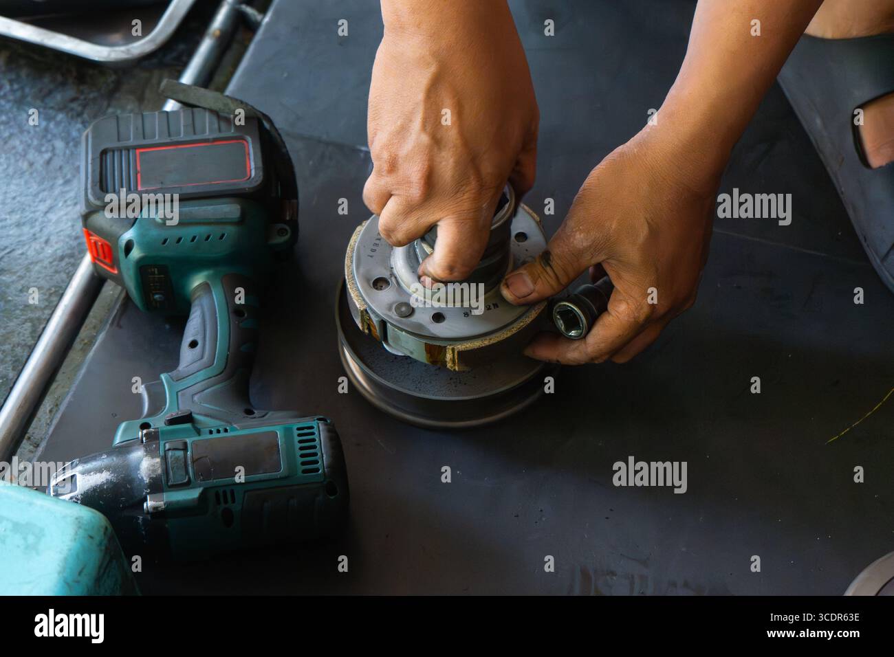 Mano del meccanico che esegue la manutenzione del sistema CVT (Continuously Variable Transmission) di uno scooter motociclo in un'officina professionale. Ideale per Foto Stock