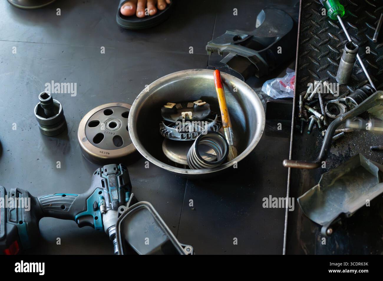 Mano del meccanico che esegue la manutenzione del sistema CVT (Continuously Variable Transmission) di uno scooter motociclo in un'officina professionale. Ideale per Foto Stock