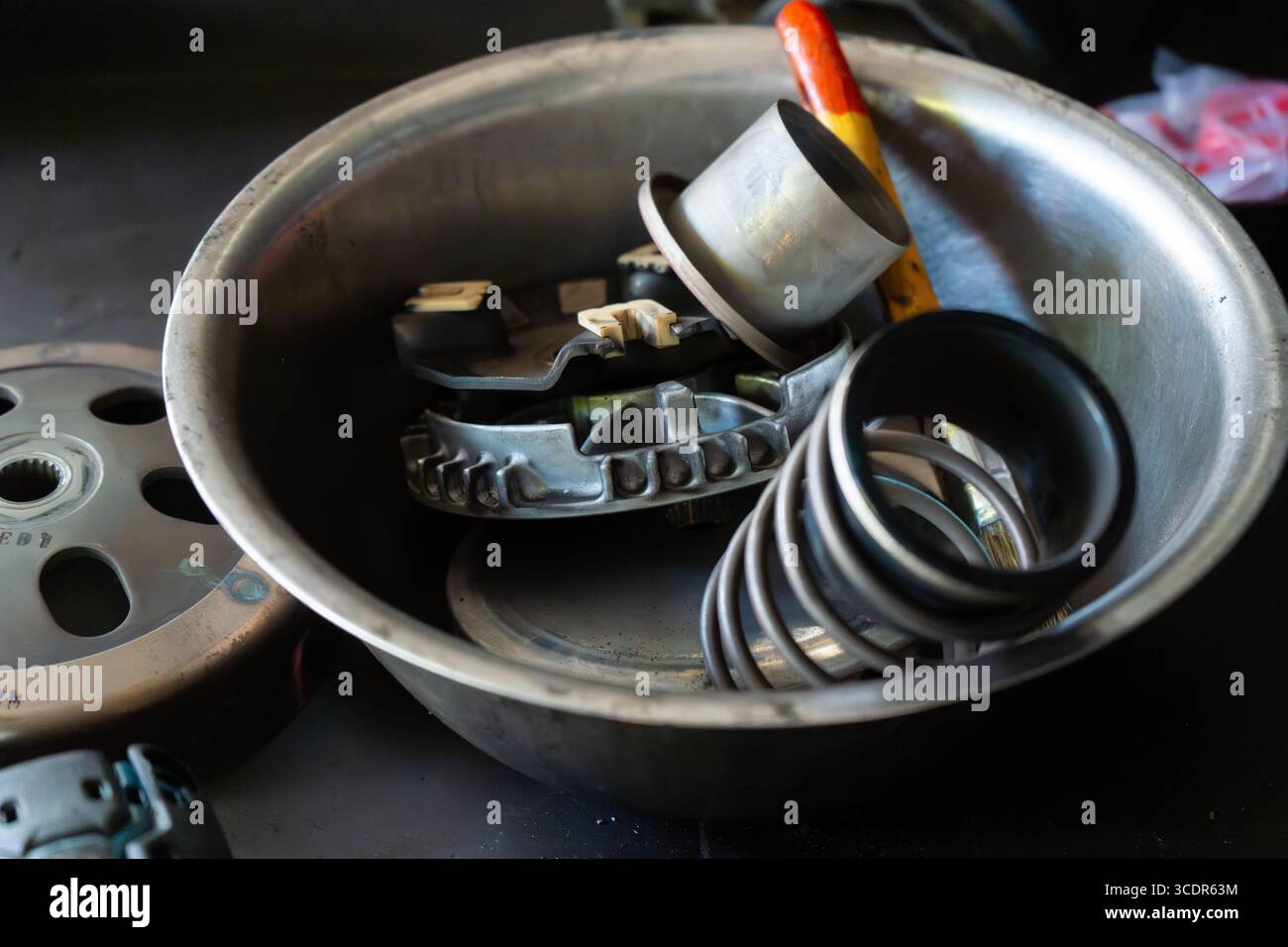 Mano del meccanico che esegue la manutenzione del sistema CVT (Continuously Variable Transmission) di uno scooter motociclo in un'officina professionale. Ideale per Foto Stock