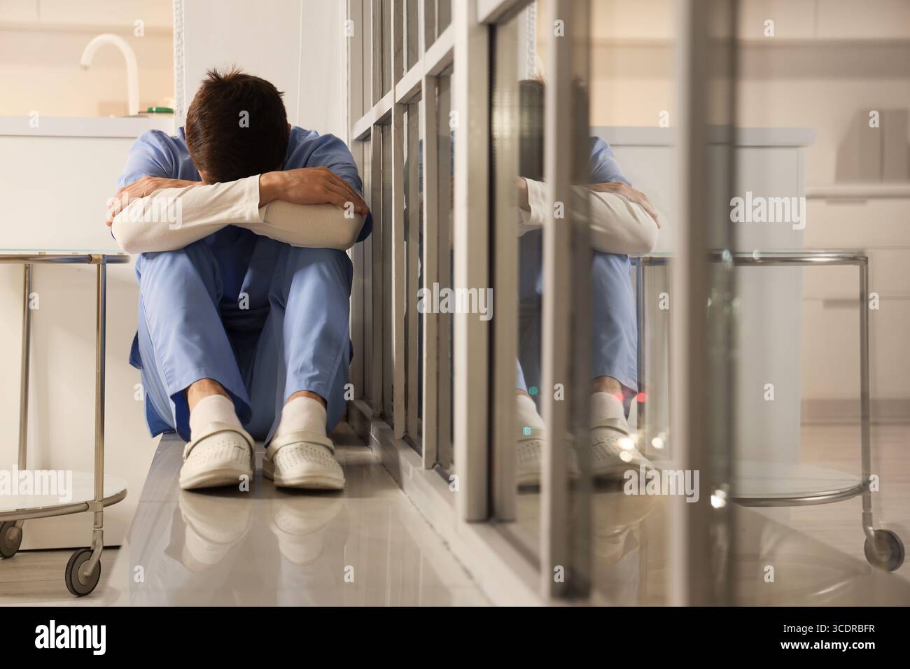Infermiera maschile stressata seduta su davanzale in ospedale di sera Foto Stock