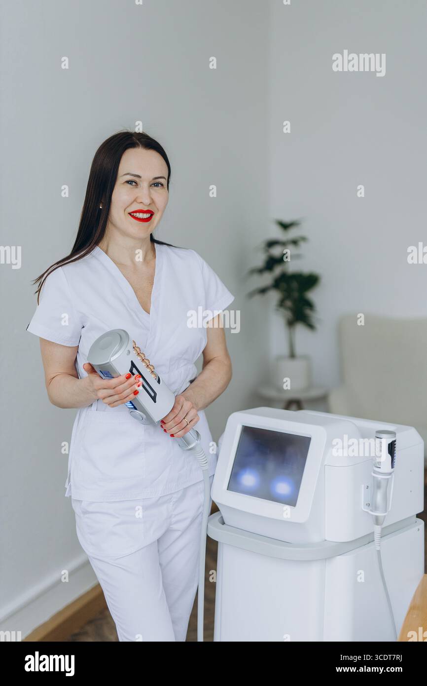 Cosmetologo sorridente che tiene in mano il dispositivo per la terapia endosferica. Attrezzature professionali per il contorno del corpo in moderne cliniche estetiche. Trattamento anti-cellulite Foto Stock