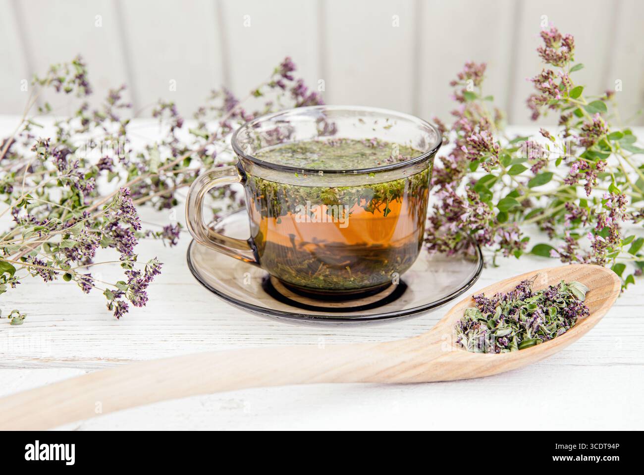 Origano fatto in casa, tè alle erbe all'Origanum vulgare in una tazza da tè. Bevanda calda al vapore con fiori freschi e secchi di origano in fiore, tavola di legno bianca. Foto Stock