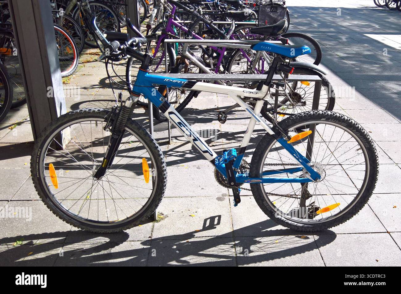 Fahrradparkplatz vor einem Supermarkt. GT Tempest, GT Bike, Mountainbike - Made in USA. GT Bicycles Inc, steht für die Initialen des Gründers Gary Turner. Er War in Seinen Anfängen ein amerikanischer Fahrradhersteller. Die Marke gehört inzwischen zum kanadischen Mischkonzern Dorel Industries *** Parcheggio biciclette di fronte a un supermercato GT Tempest, GT Bike, mountain bike made in USA GT Bicycles Inc, sta per le iniziali del fondatore Gary Turner era un produttore di biciclette americano nei suoi primi giorni il marchio ora appartiene al conglomerato canadese Dorel Industries Foto Stock