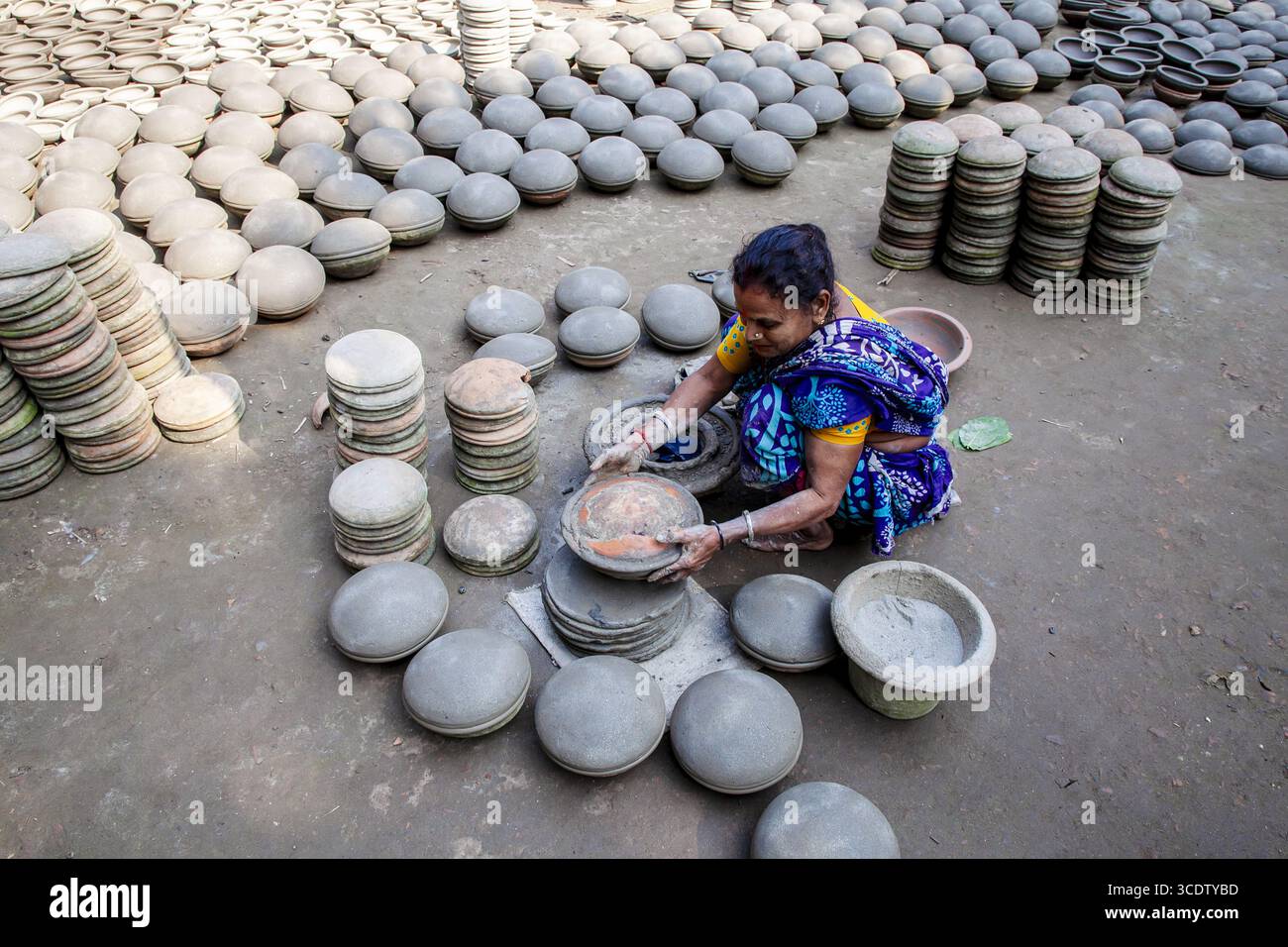 Munshiganj, Bangladesh - 23 novembre 2024: Veduta di una donna in mezzo a un mare di vasi di terra, le sue mani un turbinio di movimento, modellando e impilando con grazia praticata, sotto il cielo aperto. Foto Stock