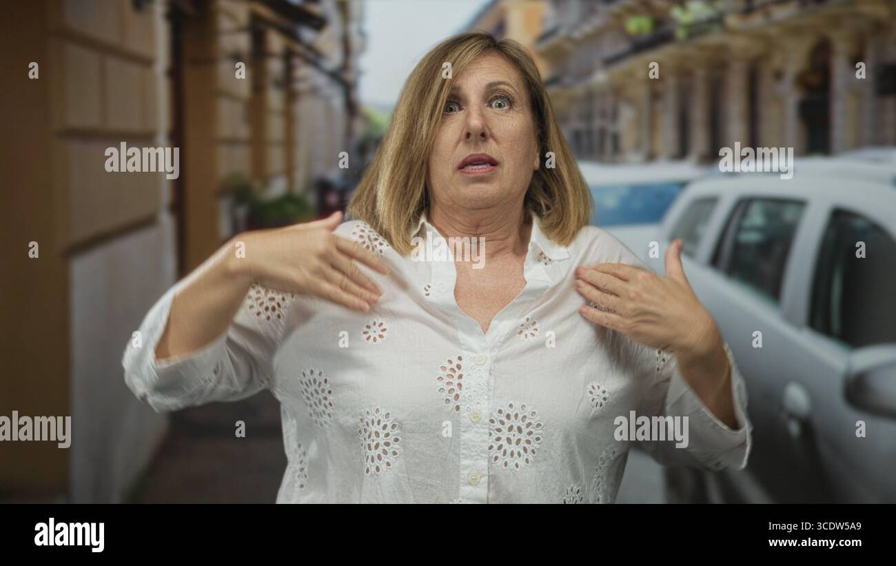Donna caucasica di mezza età che protegge gli occhi con le mani alzate su una strada urbana trafficata con auto parcheggiate; frustrazione. Foto Stock