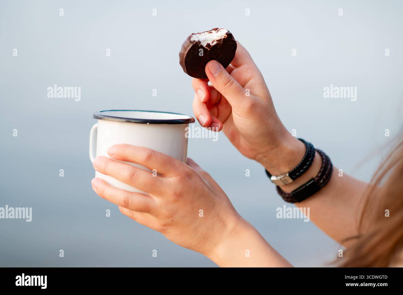 Primo piano dettagliato delle mani di una donna che tiene in mano una tazza di bevanda calda e una caramella al cioccolato, per catturare un momento accogliente e appagante Foto Stock