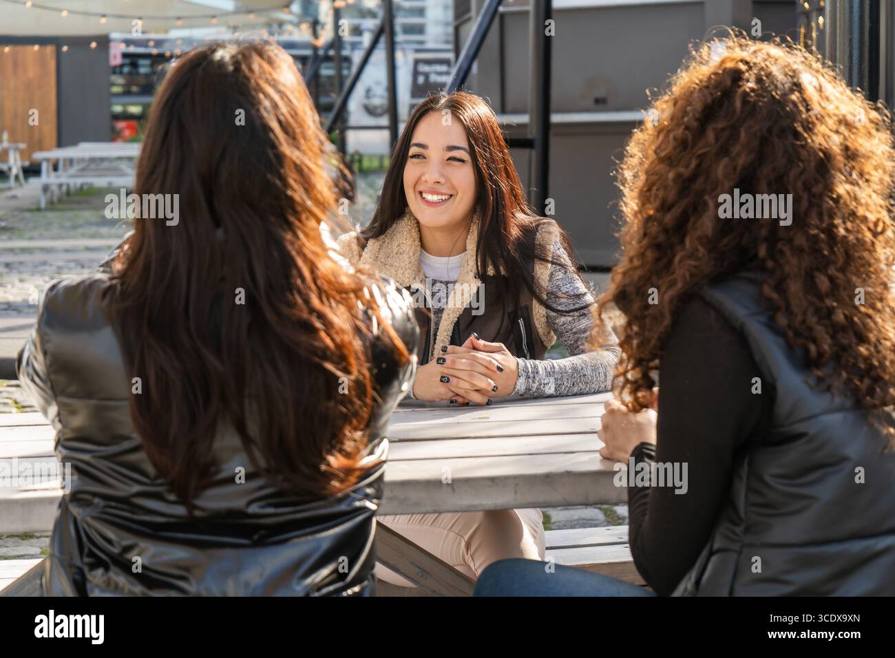Tre amiche sono sedute a un tavolo all'aperto, sorridono e parlano Foto Stock