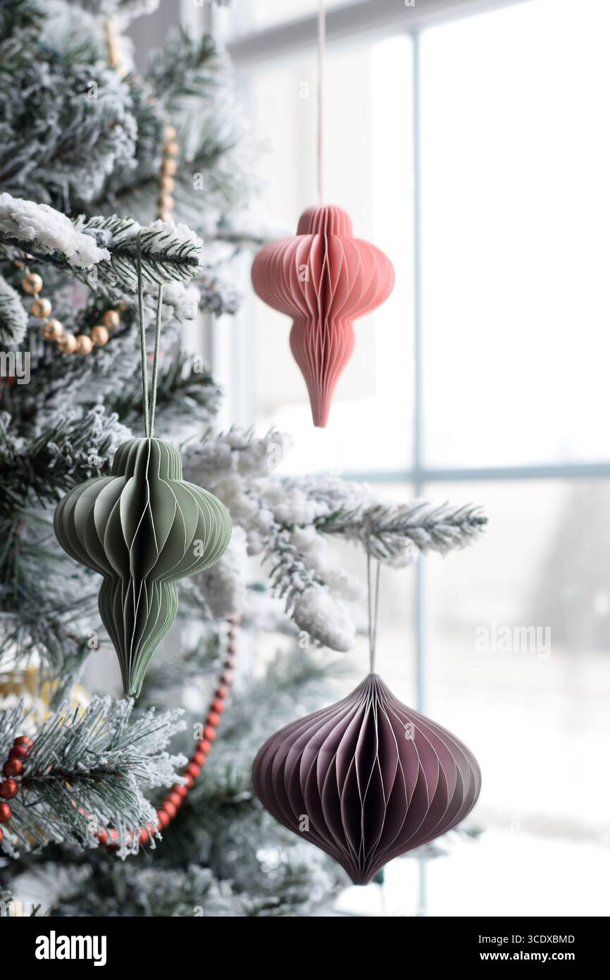 Ornamenti natalizi in carta a nido d'ape fai-da-te appesi all'albero di Natale vicino a una finestra Foto Stock