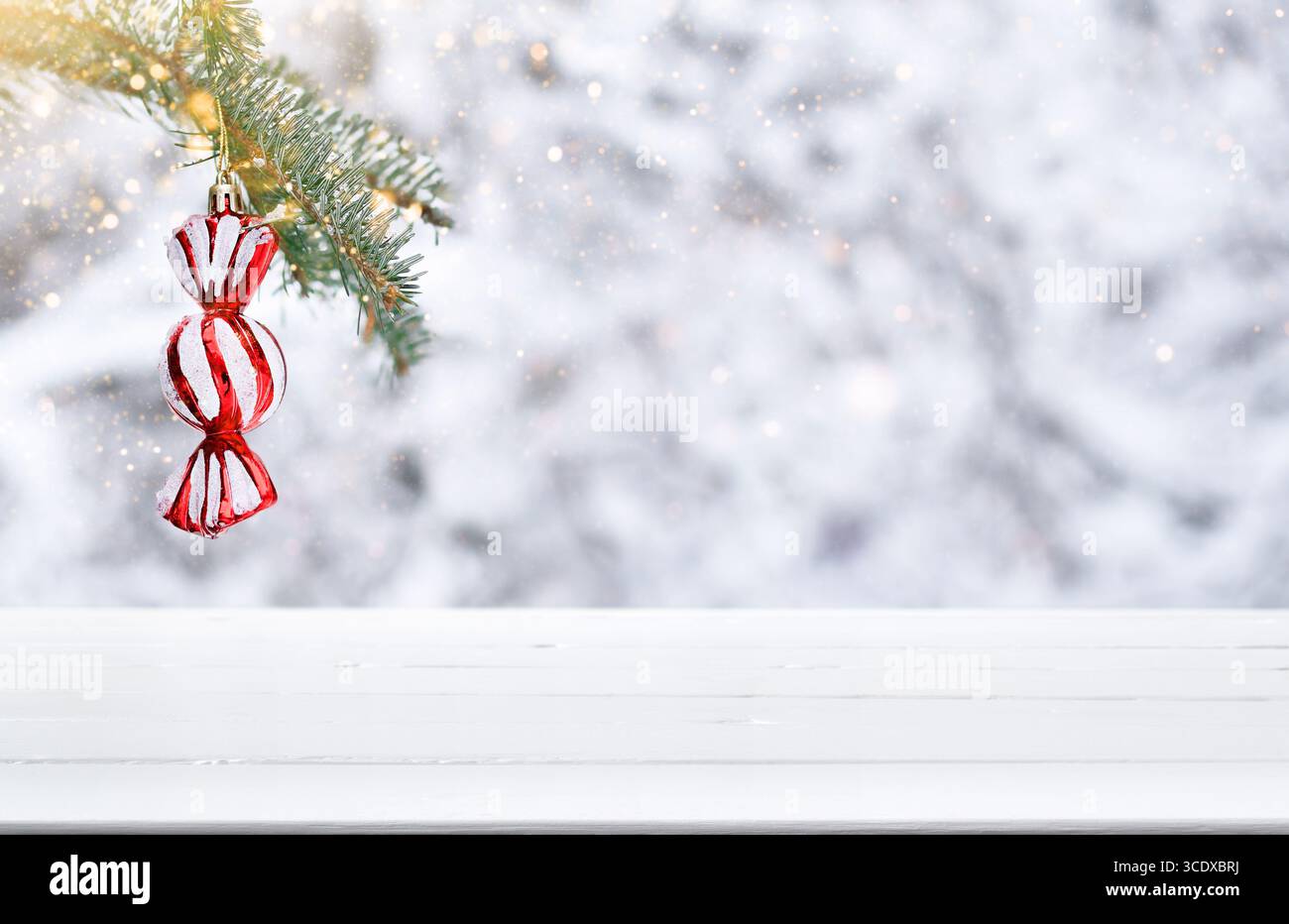 Sfondo natalizio con superficie vuota in legno bianco per il posizionamento dei prodotti, ornamento a forma di caramelle avvolte appese al ramo sempreverde Foto Stock