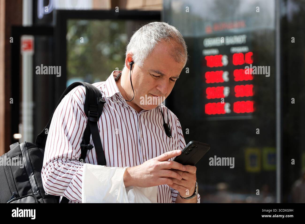 Uomo con smartphone in piedi vicino all'ufficio di cambio valuta sulla strada della città, tassi del rublo russo, dollaro statunitense Foto Stock