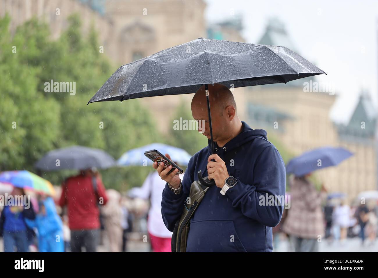 Uomo con ombrello che usa lo smartphone su una strada, piove in città estiva Foto Stock