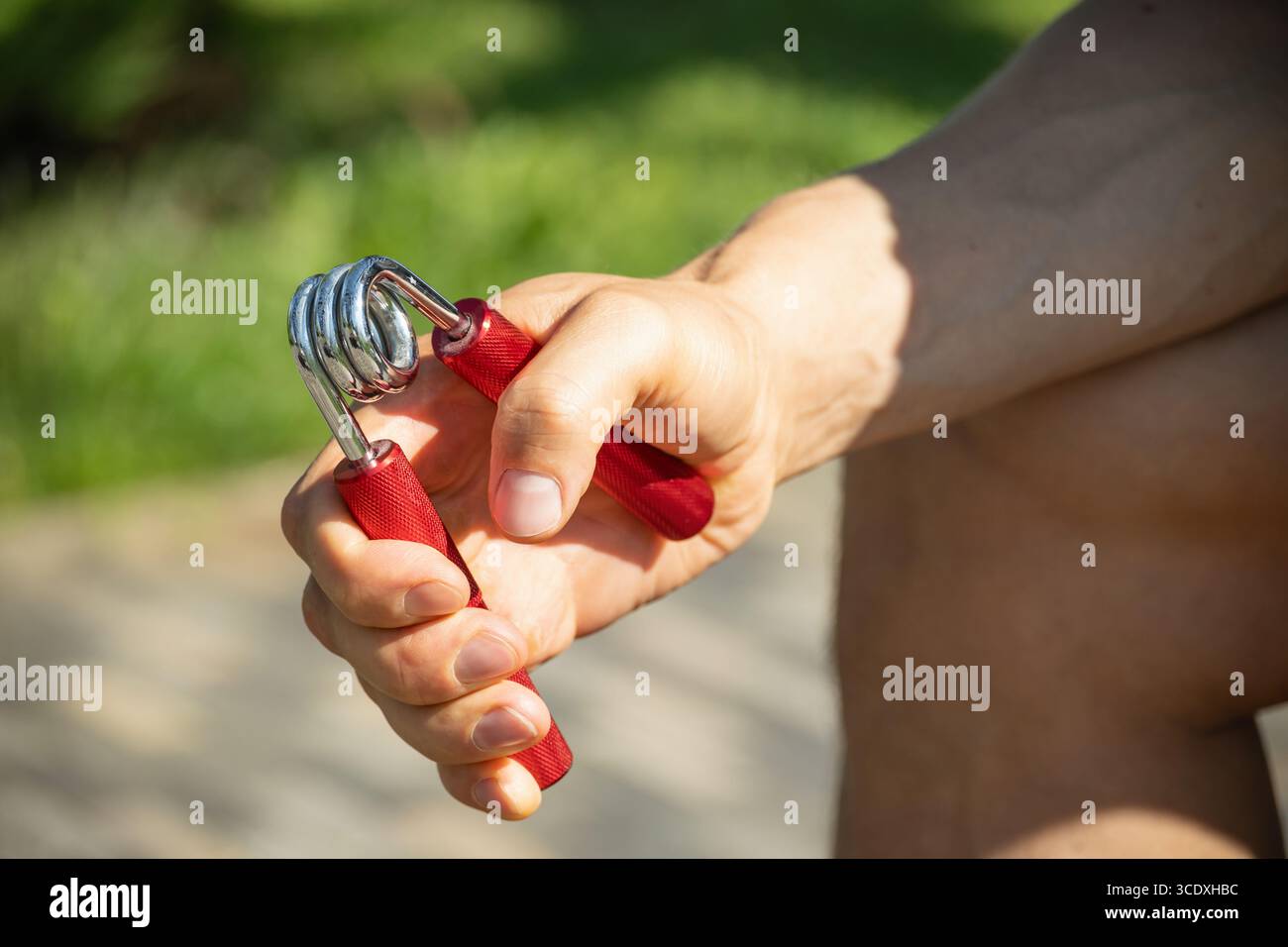 L'uomo rafforza la sua presa con un espansore in metallo rosso a mano. Si vede tenere un espansore con una presa salda, suggerendo un esercizio concentrato Foto Stock