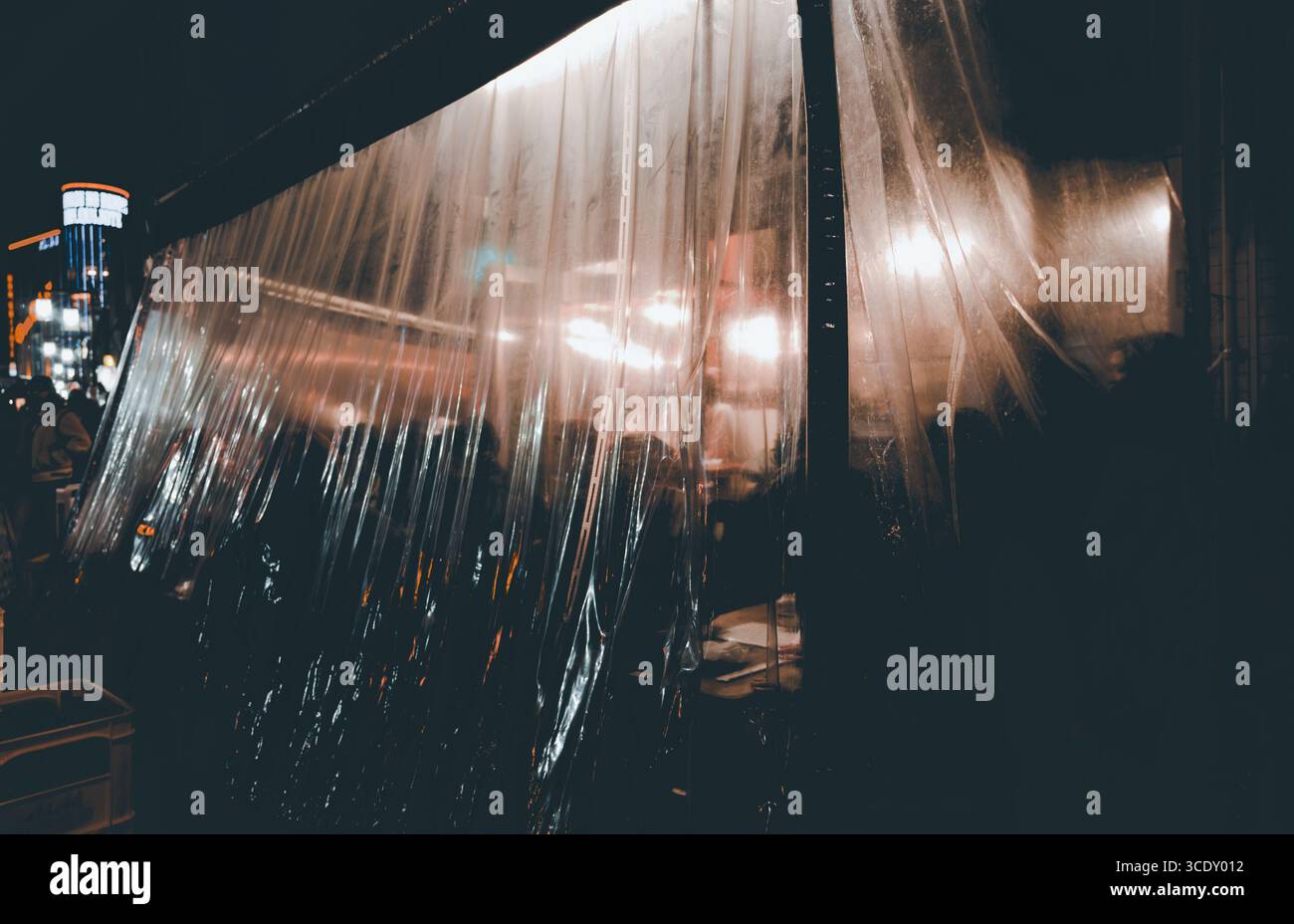 Scena gastronomica notturna ad Asakusa, un piccolo ristorante protegge i suoi vivaci tavoli esterni con tende in plastica trasparente Foto Stock