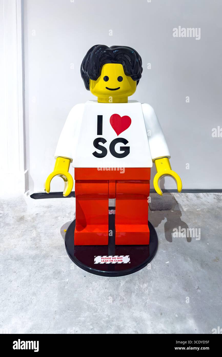 Grande personaggio in stile Lego colorato con i capelli neri che indossa una camicia "i Love SG" e pantaloni o pantaloni rossi che amo singapore - Immagine stock catturata con smartphone