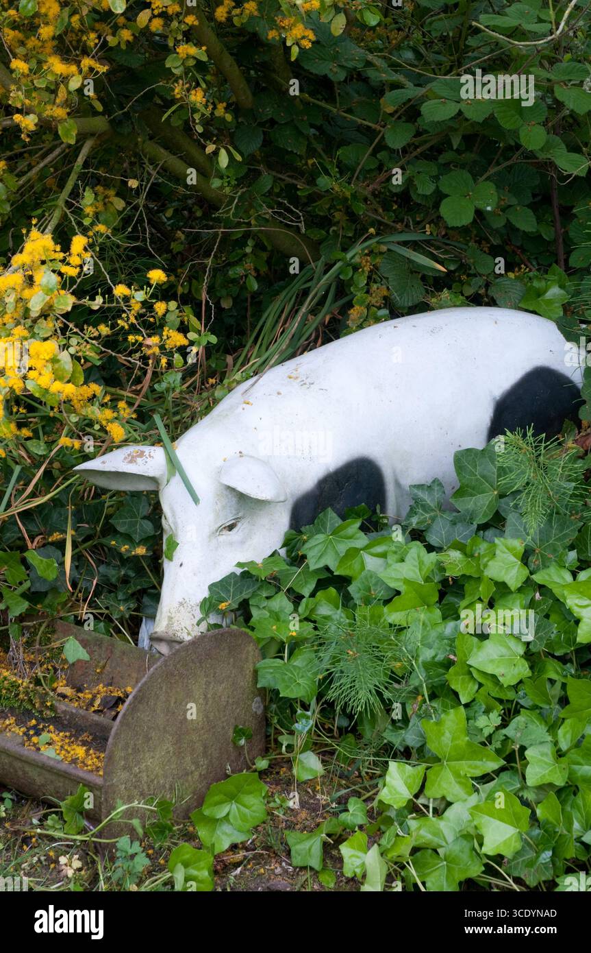 La scultura della mucca si trova tra lussureggianti piante verdi e vibranti fiori gialli, creando un punto focale orto stravagante circondato dalla natura. Foto Stock
