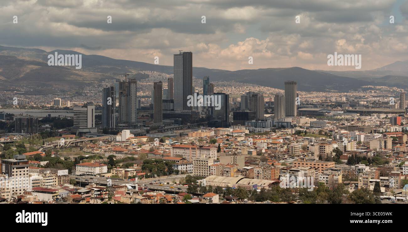 Smirne, Turchia - 6 aprile 2025: Paesaggio urbano panoramico, con grattacieli moderni, tra cui le Torri Folkart, le aree residenziali, la baia di Smirne e le montagne lontane con turbine eoliche Foto Stock