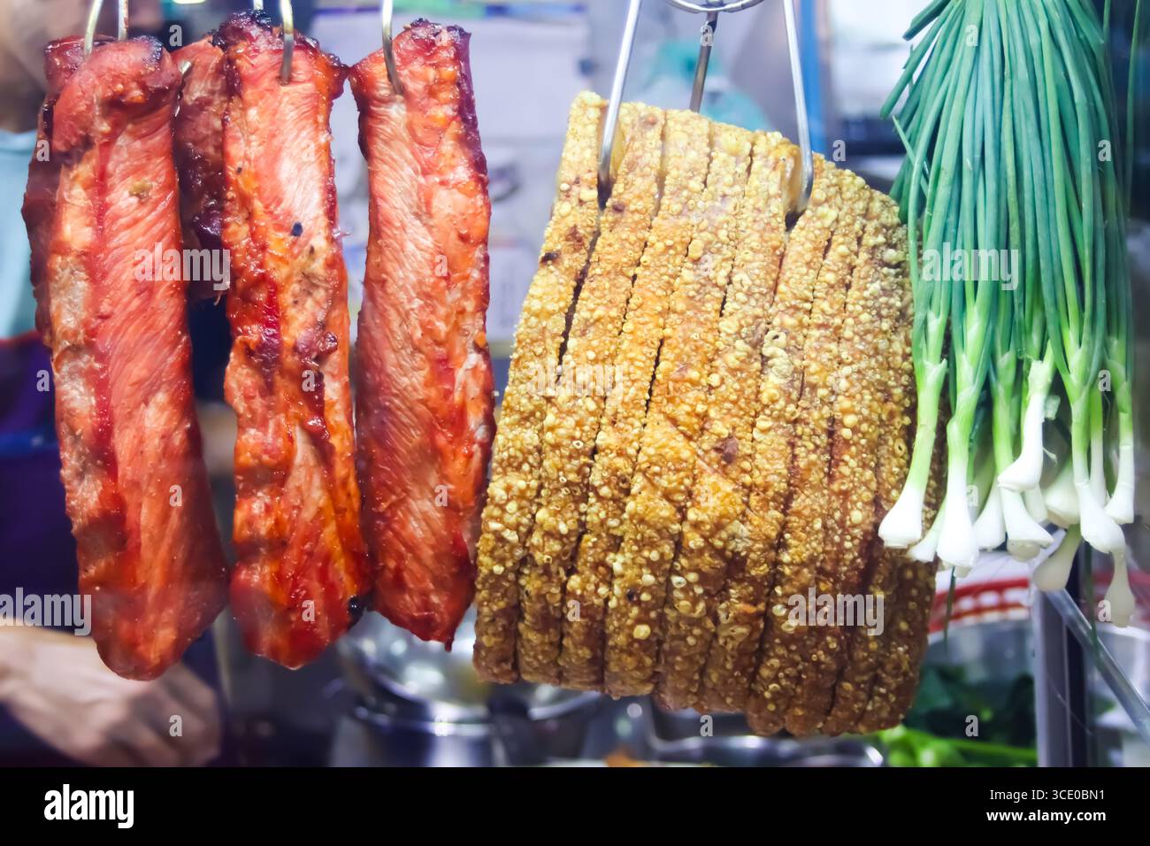Bancarelle di cibo del mercato notturno asiatico con carne di maiale siu al barbecue e pancetta croccante di maiale su ganci con scalpelli freschi, simboleggiano il vivace cibo di strada. Foto Stock