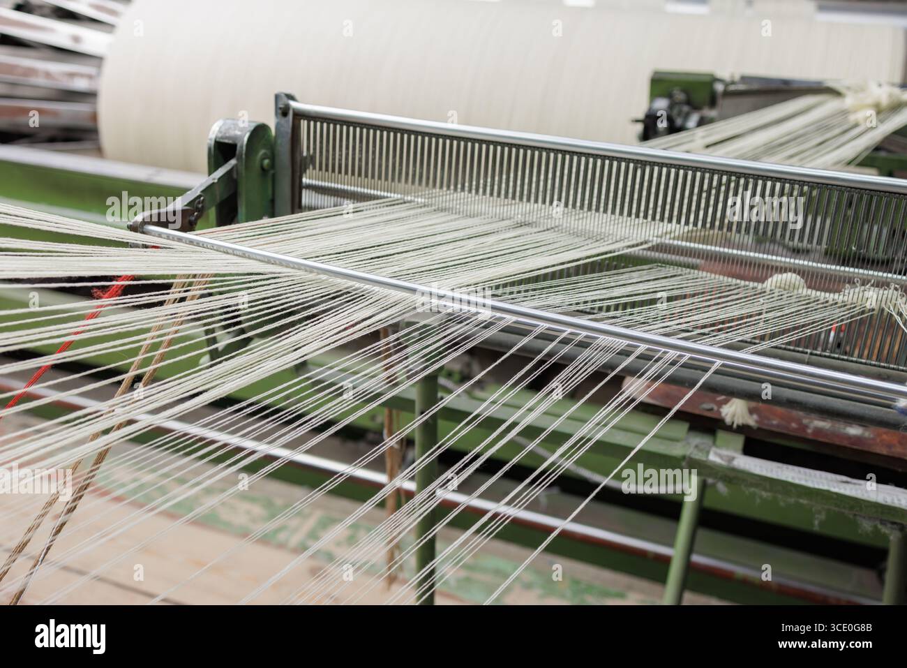I fili di ordito passano attraverso la canna su un telaio moderno, mostrando una produzione e un allineamento precisi del tessuto di lana in un mulino industriale pulito. Foto Stock