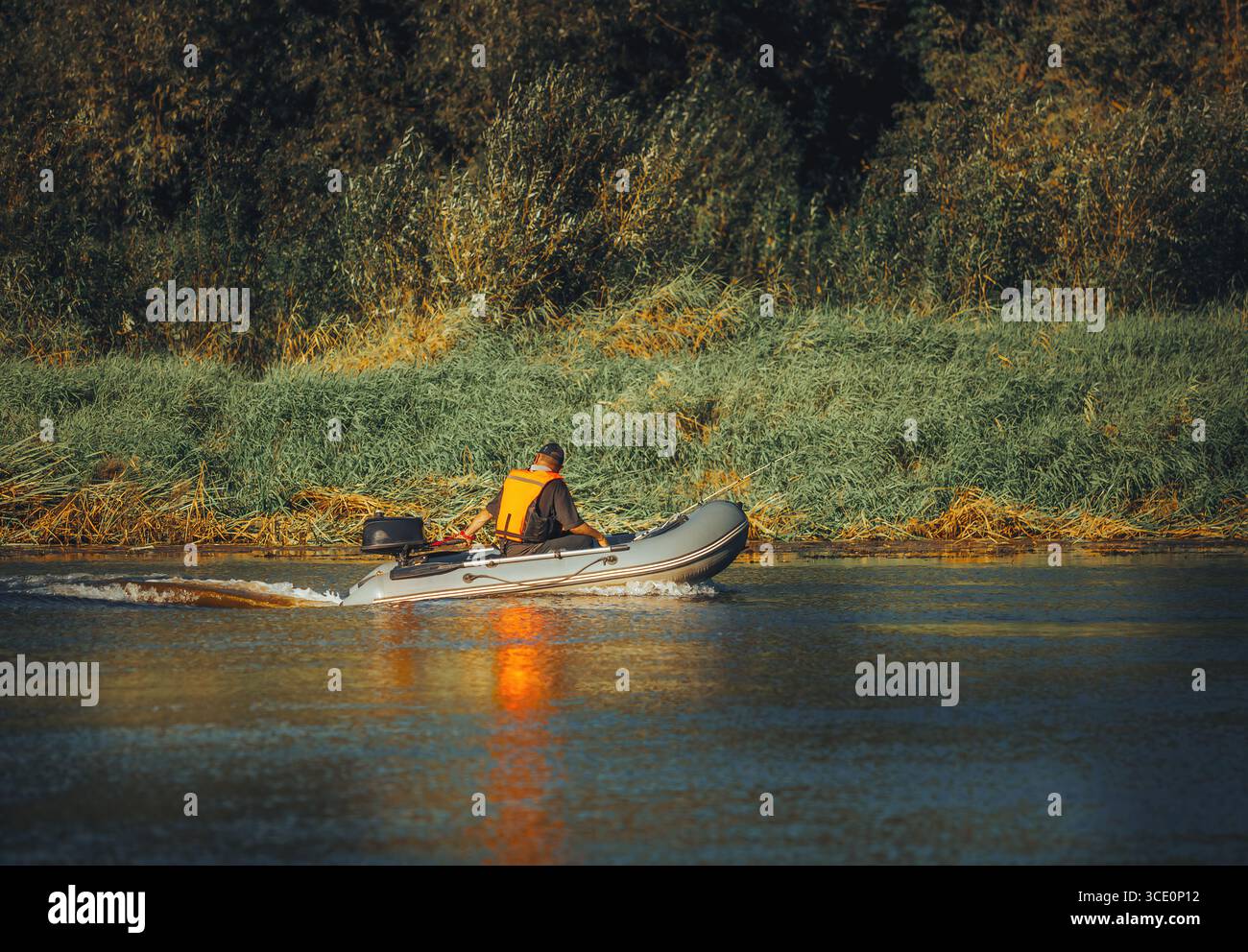 un pescatore su una barca galleggia lungo il fiume con canne da pesca Foto Stock