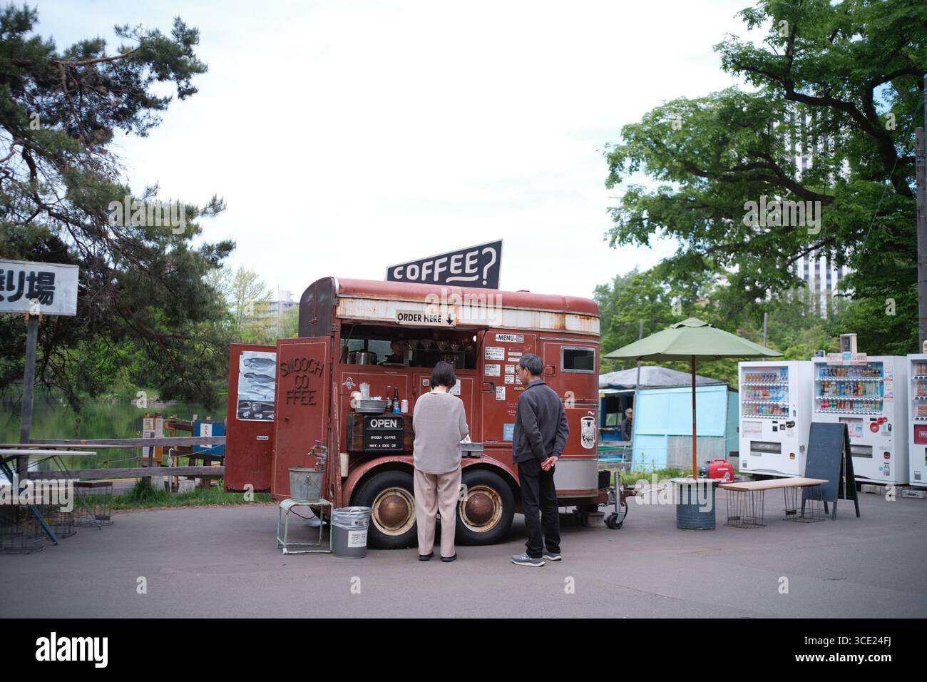 Rustico camion mobile del caffè che serve bevande in un parco all'aperto a Sapporo, in Giappone, con distributori automatici, alberi verdi e persone che ordinano al banco Foto Stock