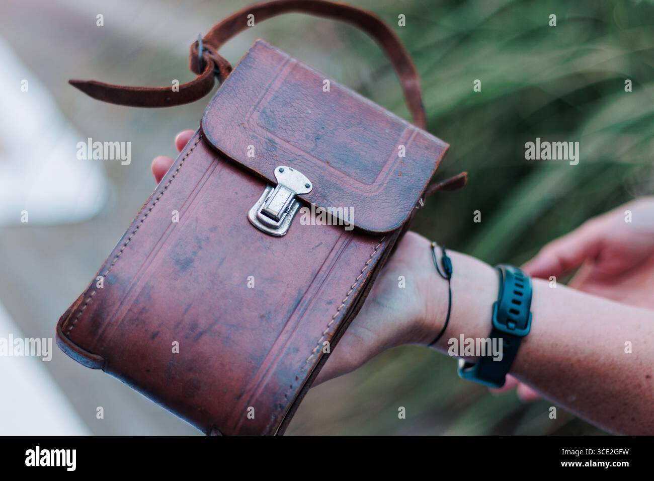 Il braccio di una persona che regge una valigia, una borsa di pelle, da una vecchia fotocamera retrò Foto Stock