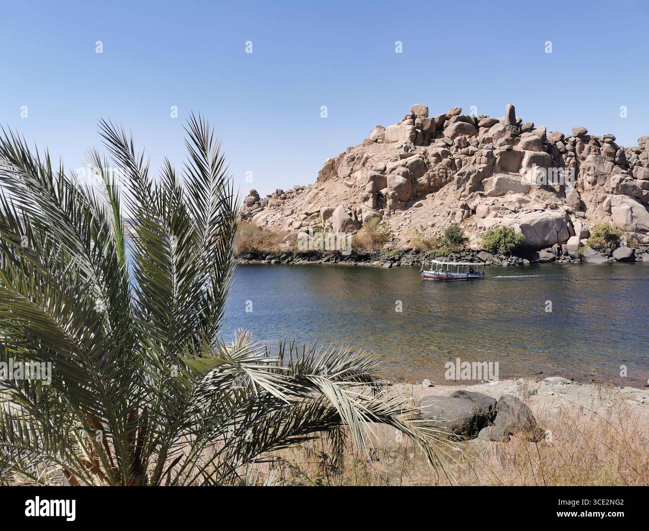 La barca turistica passa davanti a grandi isole di granito vicino al Tempio di Philae, Assuan, parzialmente sommersa dall'innalzamento delle acque del Nilo dalla diga britannica. Foto Stock