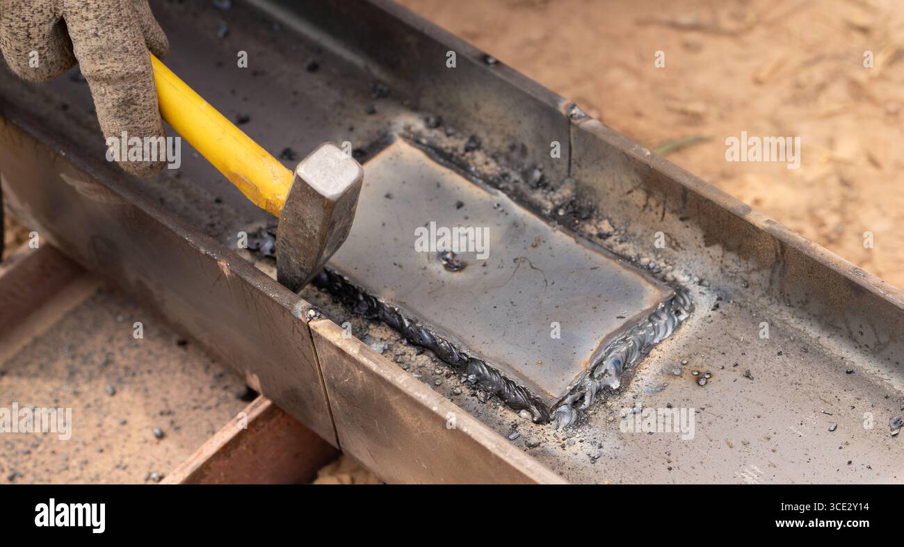 L'operaio esperto martelli la saldatura a caldo dei metalli in officine industriali, catturando l'arte della lavorazione dei metalli, la precisione della lavorazione artigianale e le scintille Foto Stock