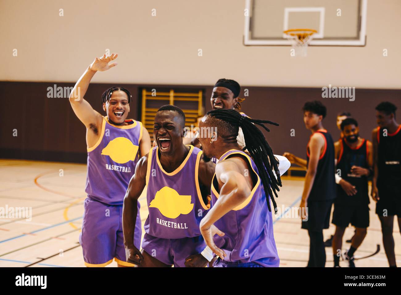 Un gruppo di giocatori di basket in maglie esprime entusiasmo e gioia dopo aver vinto una partita in un campo al coperto, mostrando il lavoro di squadra e la felicità. Foto Stock