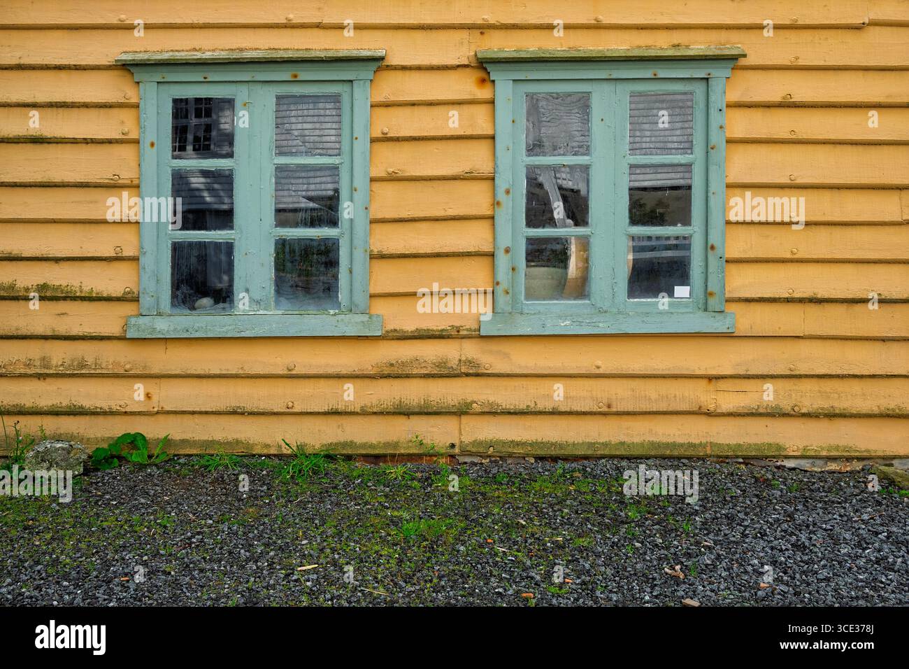 Due finestre con cornici turchesi adornano una parete gialla intemprata, che mostra la bellezza rustica di un vecchio edificio in un ambiente sereno. Foto Stock
