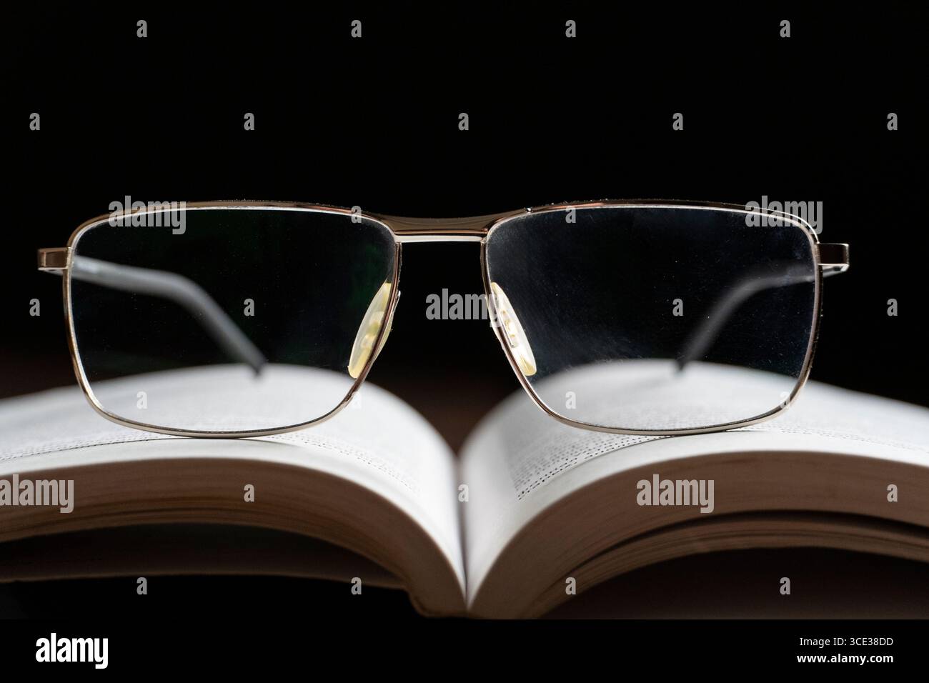 Un paio di occhiali che poggiano su un libro aperto, simboleggiano la lettura e l'apprendimento. Lo sfondo scuro migliora la messa a fuoco sugli occhiali e sulle pagine, creando Foto Stock