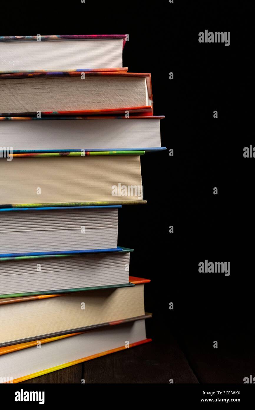 Una pila verticale di spessi libri in copertina rigida con rilegature colorate, posizionati su uno sfondo nero. Ideale per i temi dell'istruzione, della lettura e delle biblioteche Foto Stock