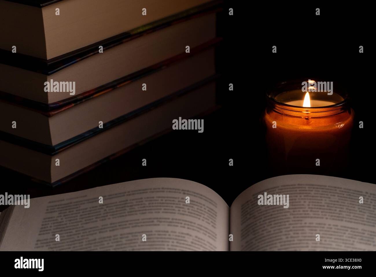 Primo piano di un libro aperto, candela accesa e libri impilati sullo sfondo. Perfetto per temi di studio, lettura, solitudine e serenità Foto Stock