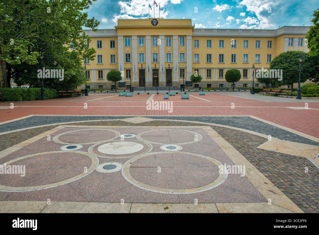 Edificio del municipio con una facciata gialla e un design decorativo della pavimentazione nella piazza principale di Nagykanizsa, in Ungheria, in un giorno estivo parzialmente nuvoloso. Foto Stock