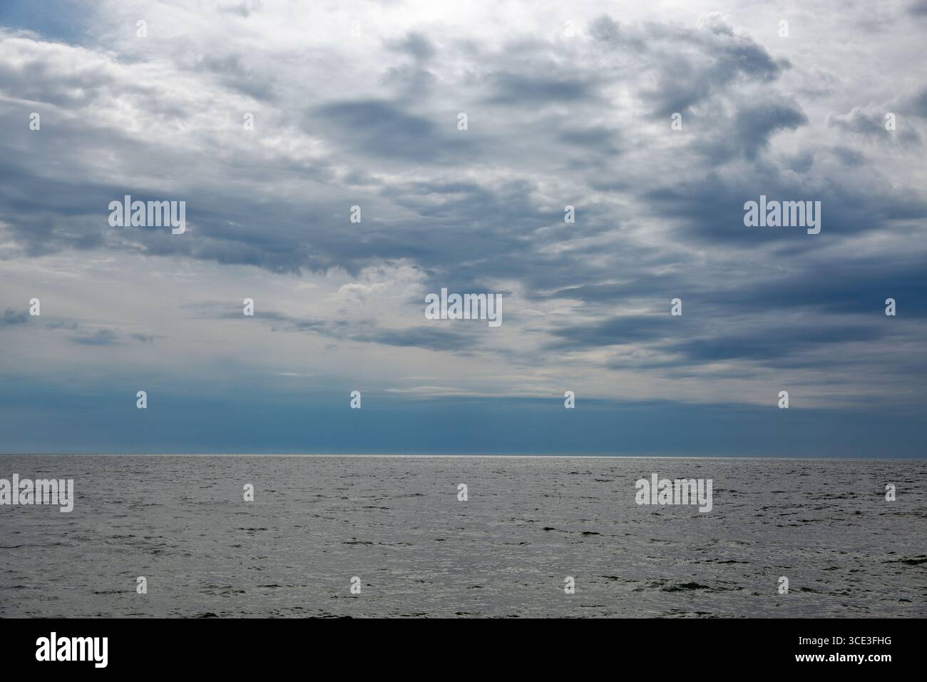 Sereno paesaggio marino con onde dolci sulla superficie dell'acqua scura che si estende fino all'orizzonte lontano sotto un cielo blu parzialmente nuvoloso con nuvole bianche e soffici. Foto Stock