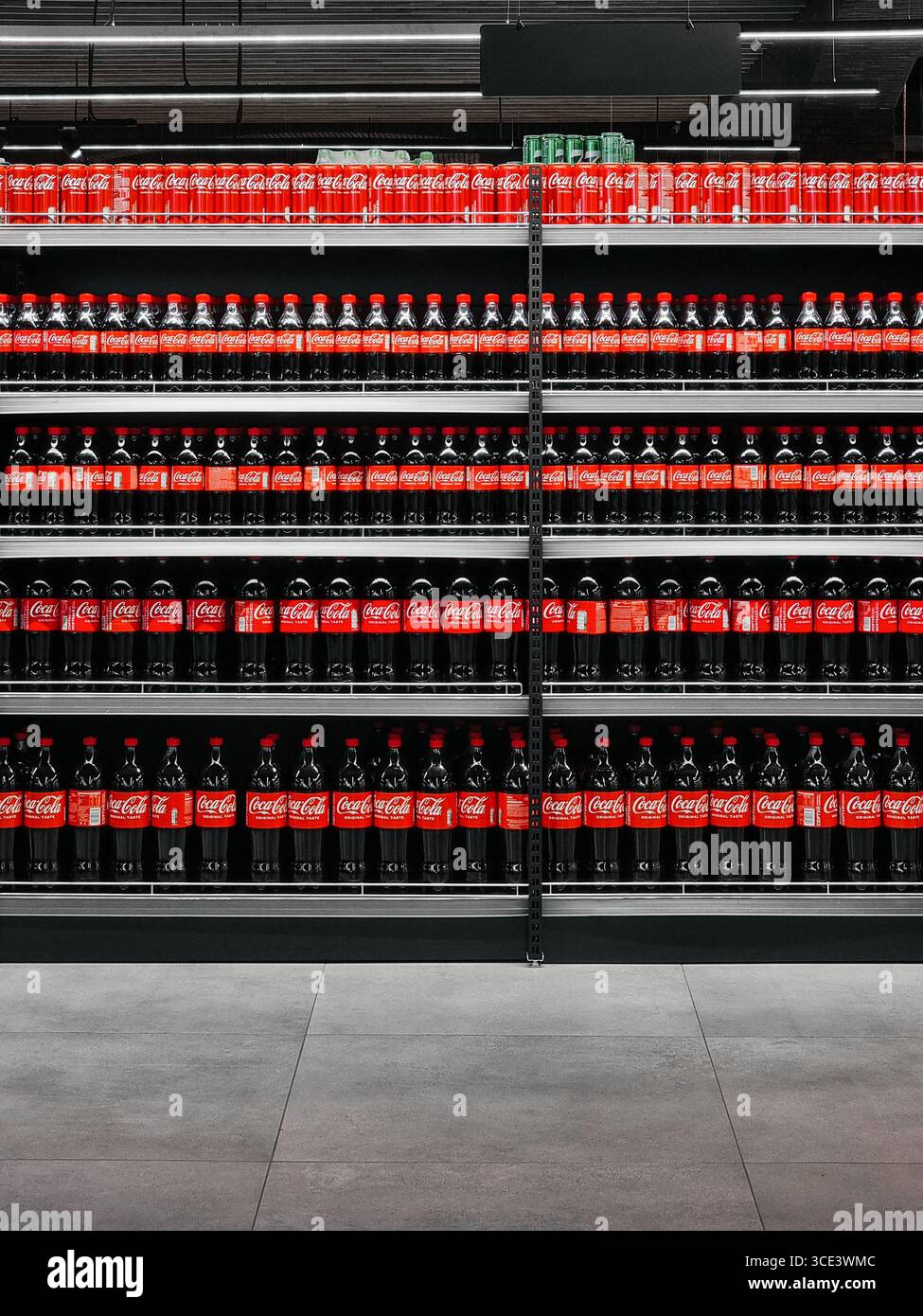 File di bottiglie di cola in vendita su rack. Guardando direttamente gli scaffali pieni di bottiglie di coca cola di diverse dimensioni all'interno di un moderno supermercato. Foto Stock