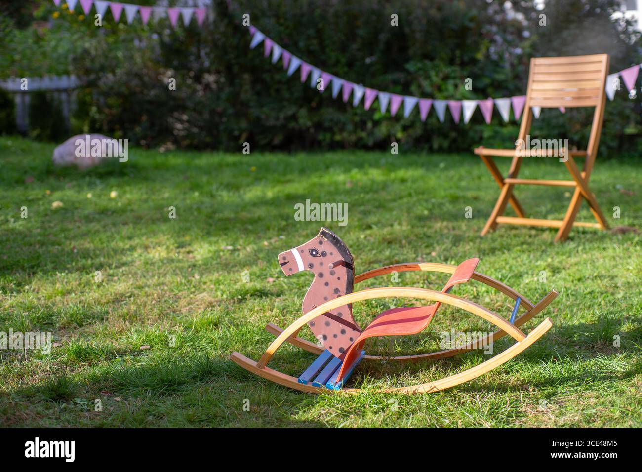 Cavallo a dondolo in legno sull'erba durante una festa all'aperto con decorazioni a grappolo. Foto Stock
