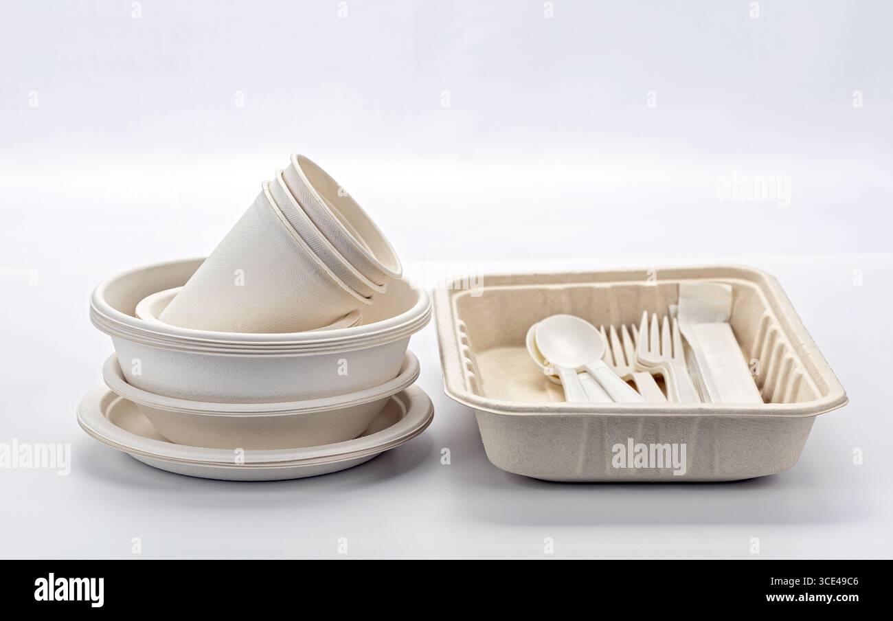 Un set di piatti, tazze e posate biodegradabili visualizzato su sfondo bianco, con stoviglie monouso ecologiche. ideale per un ambiente sostenibile Foto Stock