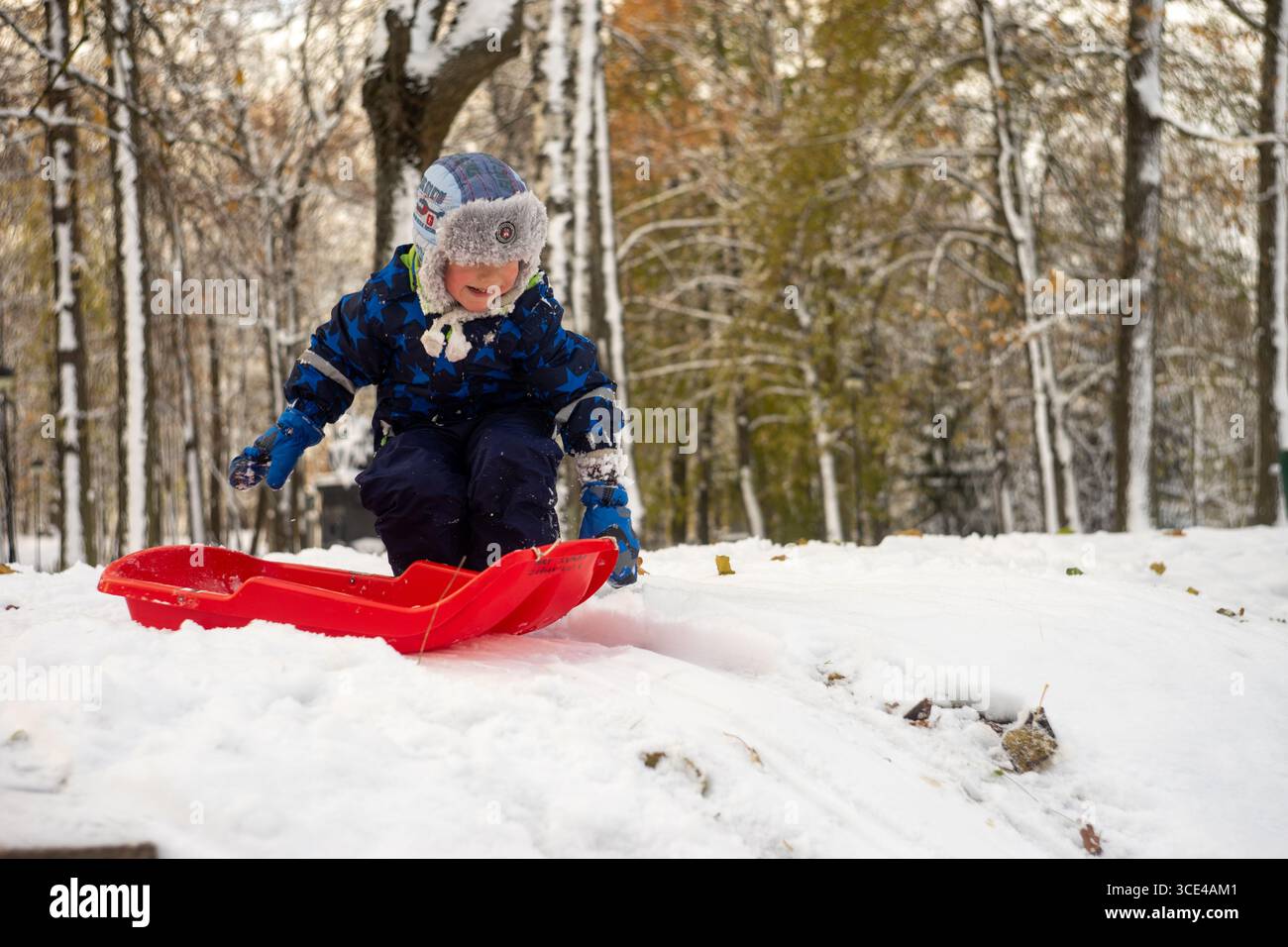 05.11.2016, Tartu, Estonia: Bambino sorridente che tira la slitta rossa in salita in una giornata invernale innevata. Foto Stock