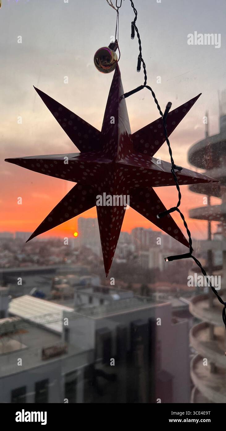 Tramonto sulla città riflesso in una finestra di vetro colorato con illuminazione blu sotto il soffitto, arredamento rosso cartapesta natalizia. Foto Stock