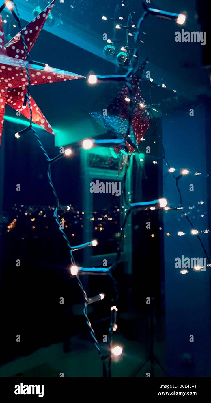 Luci notturne riflesse in una finestra in vetro colorato con illuminazione blu sotto il soffitto, decorazioni in cartapesta rossa natalizia. Foto Stock