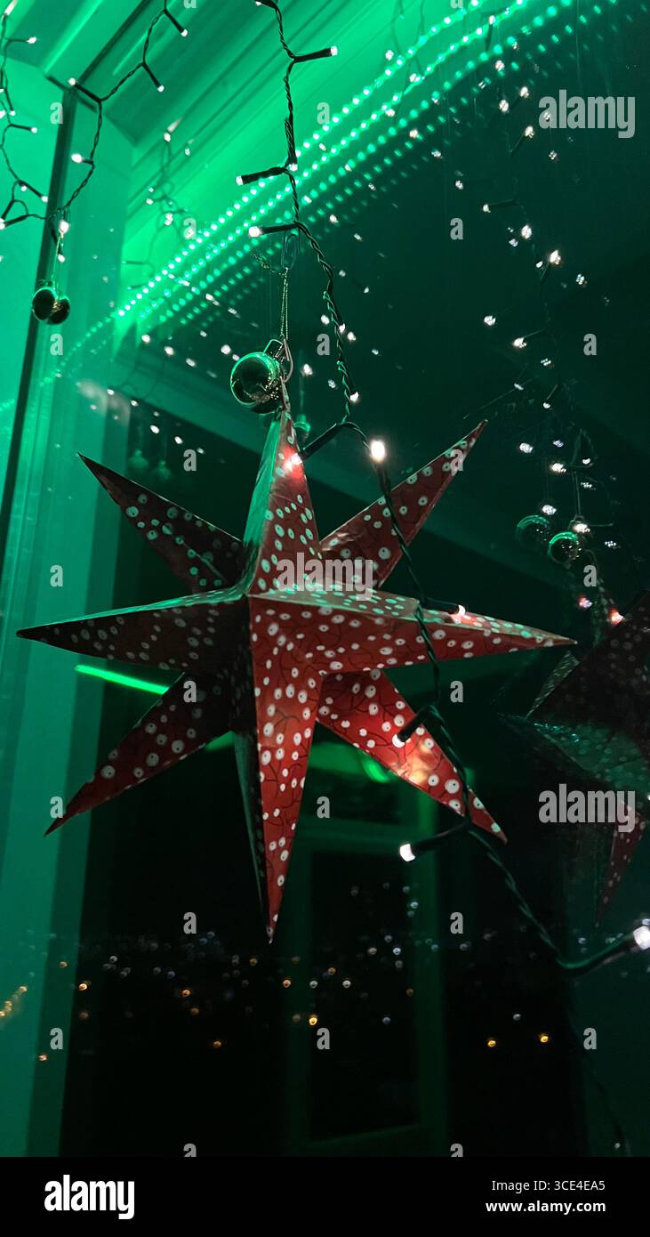 Luci notturne riflesse in una vetrata colorata con illuminazione verde sotto il soffitto, decorazioni rosse con stelle natalizie. Foto Stock