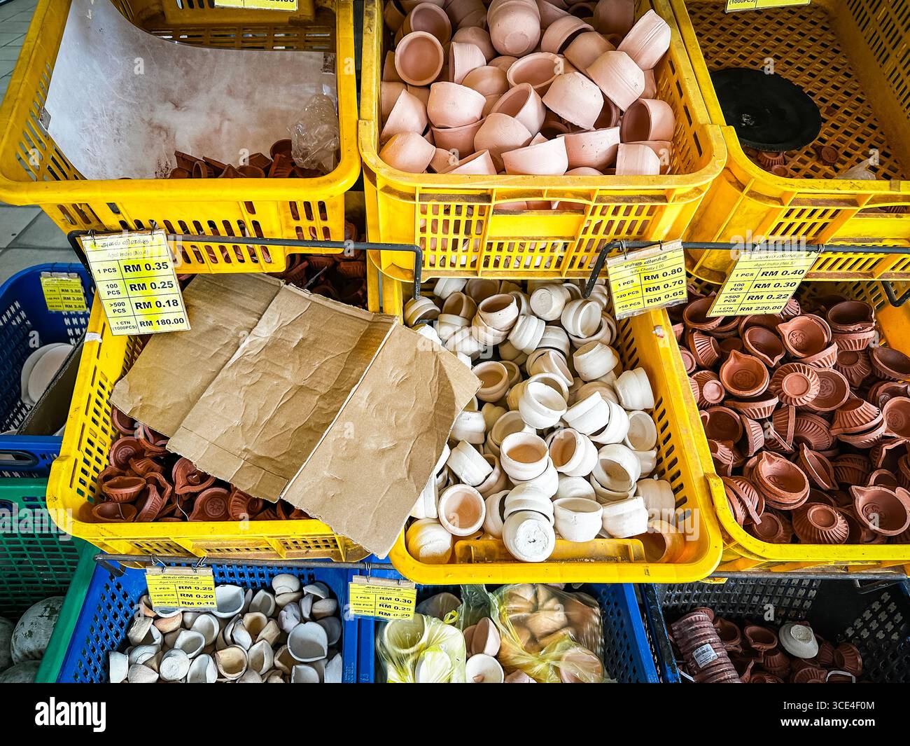 Un assortimento di piccole pentole di diya indiana tradizionali in argilla o lampade a olio esposte in casse di plastica gialle in un mercato indiano Little india malesia Foto Stock