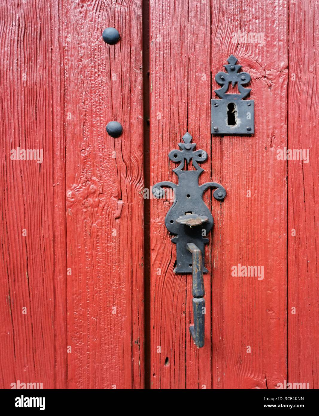 Una suggestiva porta rossa in legno presenta intricati dettagli in metallo nero e una serratura vintage. La struttura resistente alle intemperie della portiera aggiunge carattere. Francia - Immagine stock catturata con smartphone