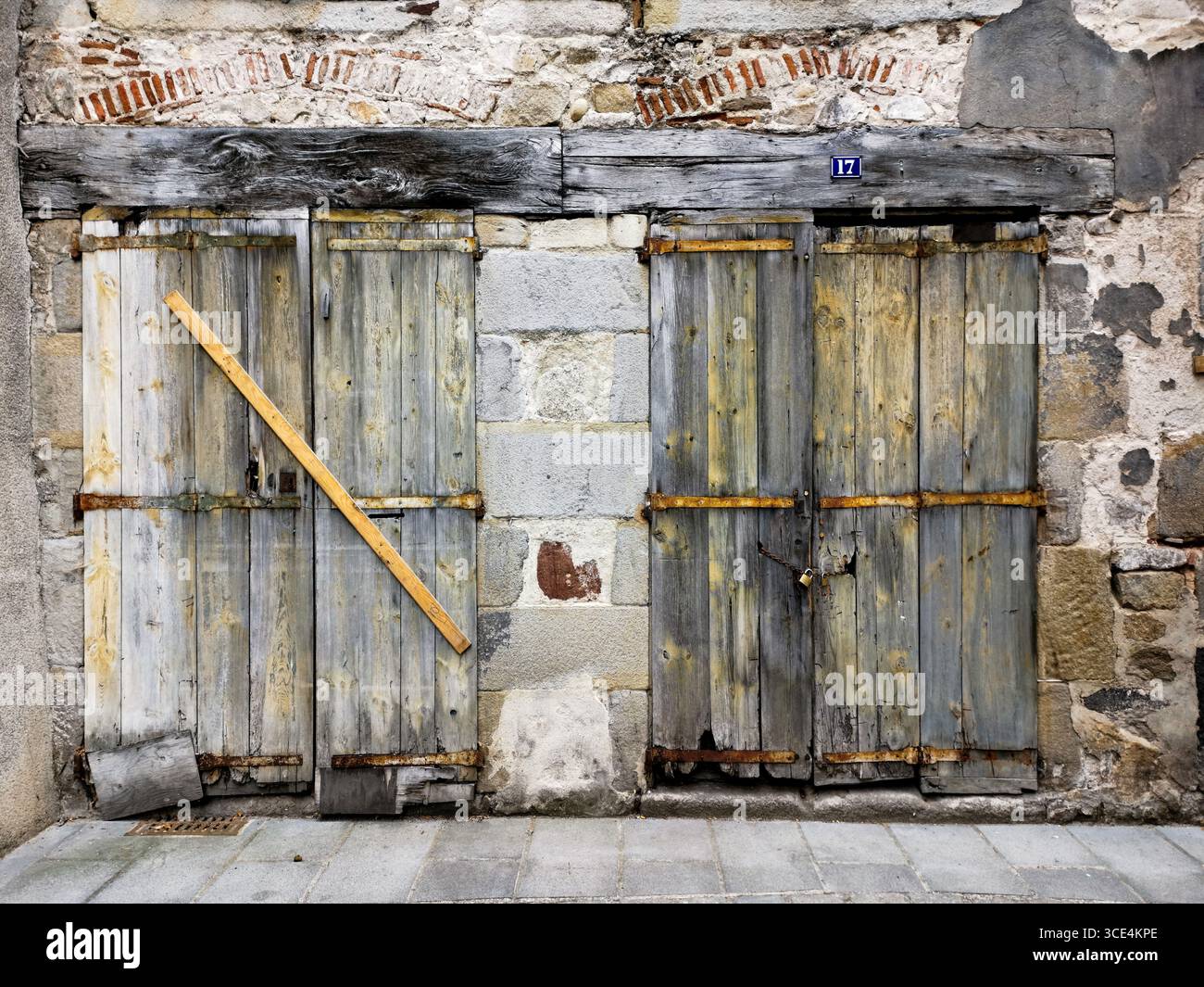 Due porte in legno intemperie fissate con una trave angolata contro un muro di pietra strutturata in una stretta strada vecchia. - Immagine stock catturata con smartphone