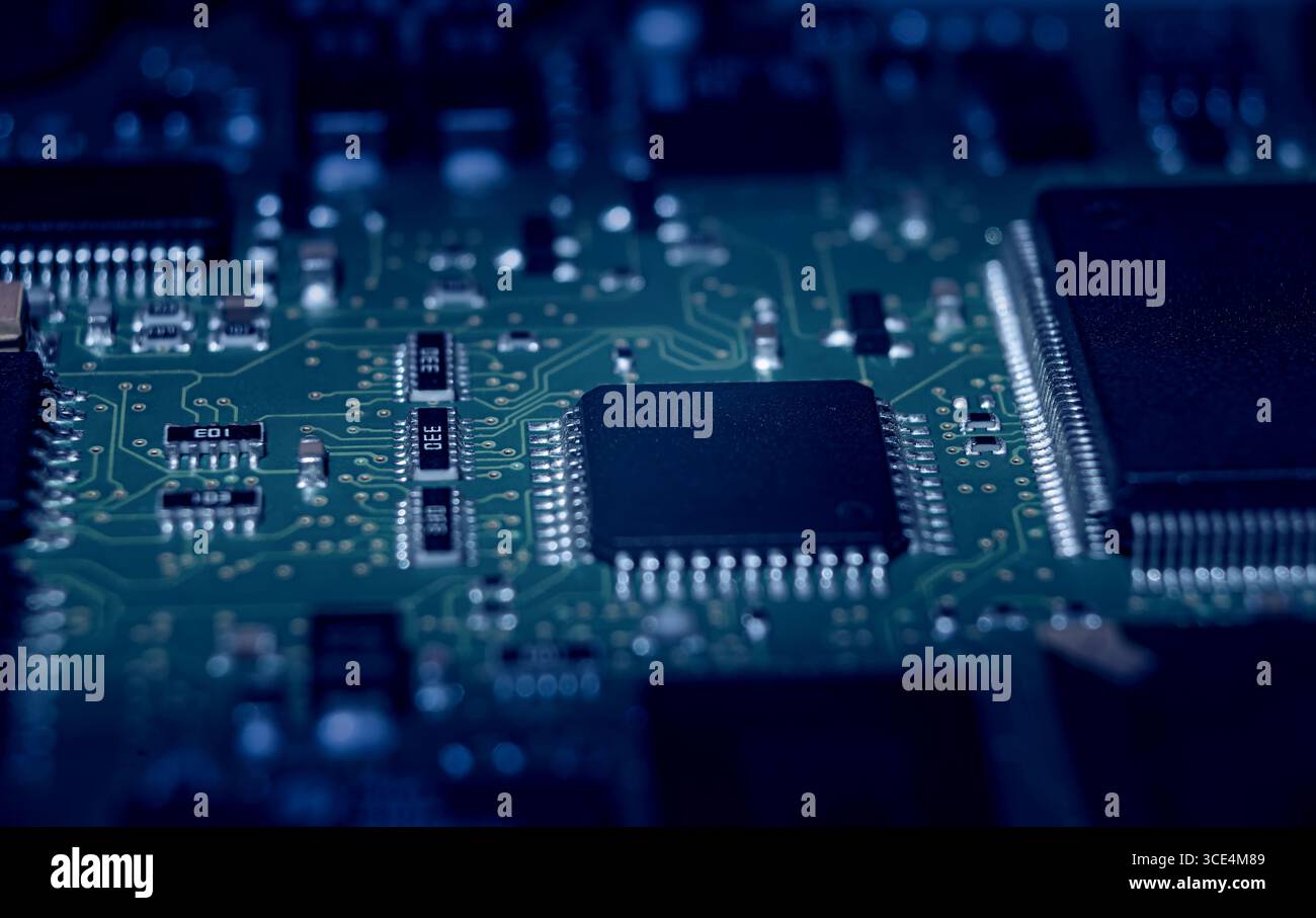L'esame dettagliato di microchip e circuiti su una scheda elettronica illustra la complessità della tecnologia e del design moderni di notte. Foto Stock