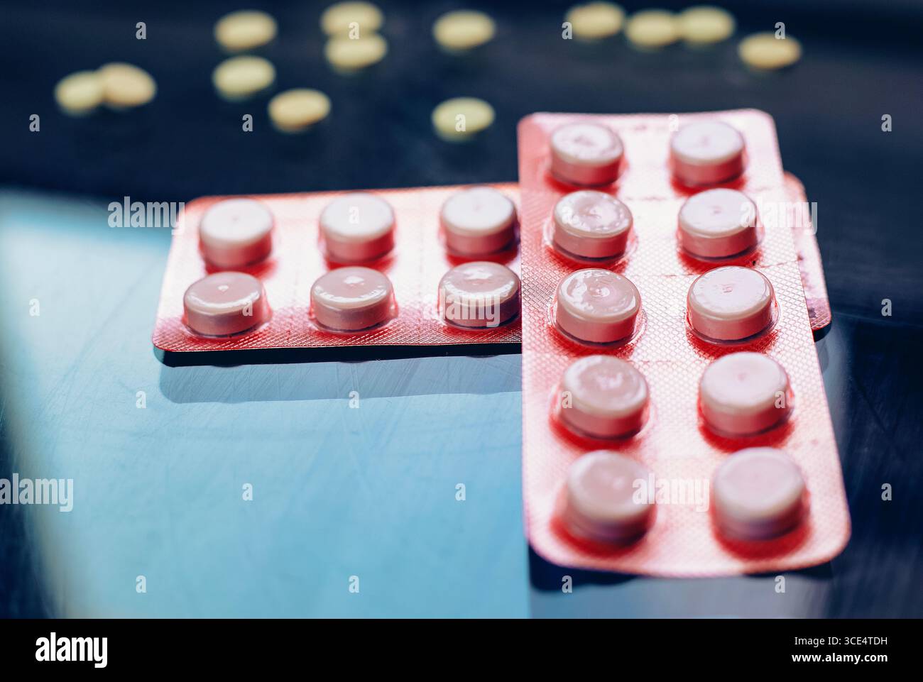 Le confezioni blister di varie pillole, incluse quelle arancioni e rosa, sono esposte contro una superficie riflettente. Alcune pillole gialle sfuse sono sparse in t Foto Stock
